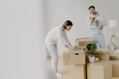 Jeune couple emménage avec cartons et chat, cherche idées déco et conseils achat maison sécurisés.