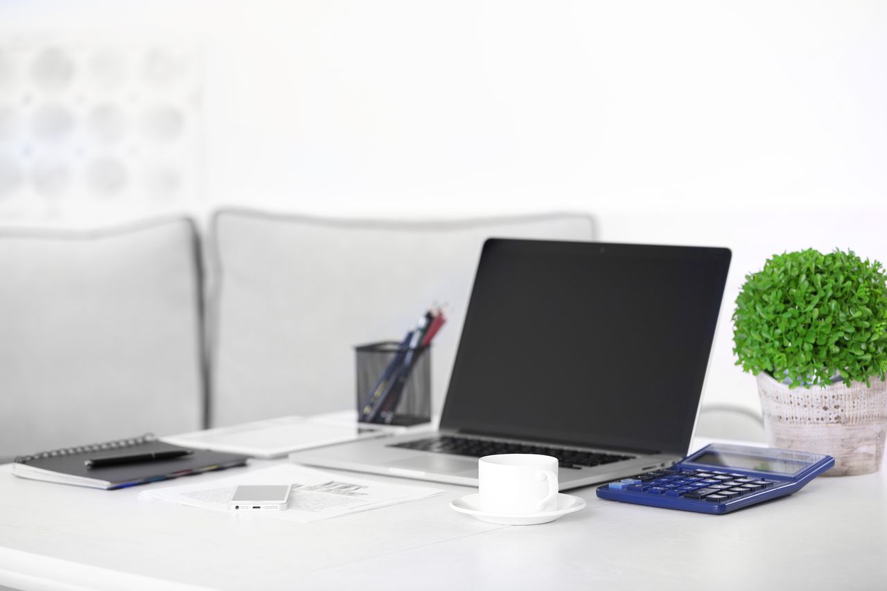 Bureau de télétravail moderne avec ordinateur portable, écran, multiprise et contrat d’assurance à proximité.