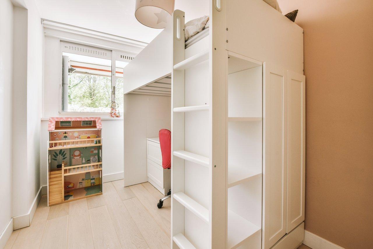 Chambre d’enfant compacte avec un lit loft, rangements muraux et coin bureau pour optimiser l’espace.