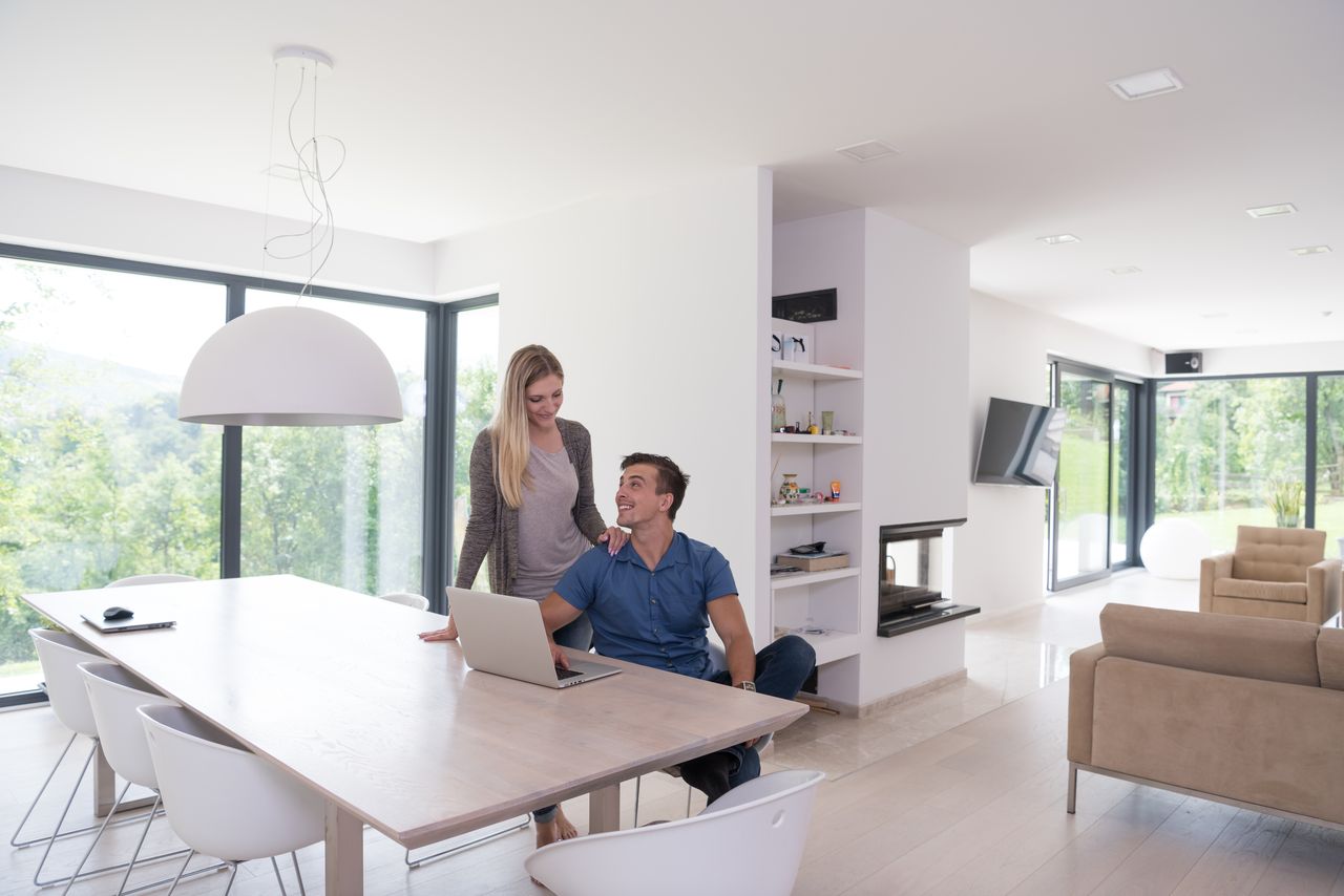 Couple consultant des documents fiscaux dans une maison neuve contemporaine avec ordinateur portable sur la table.
