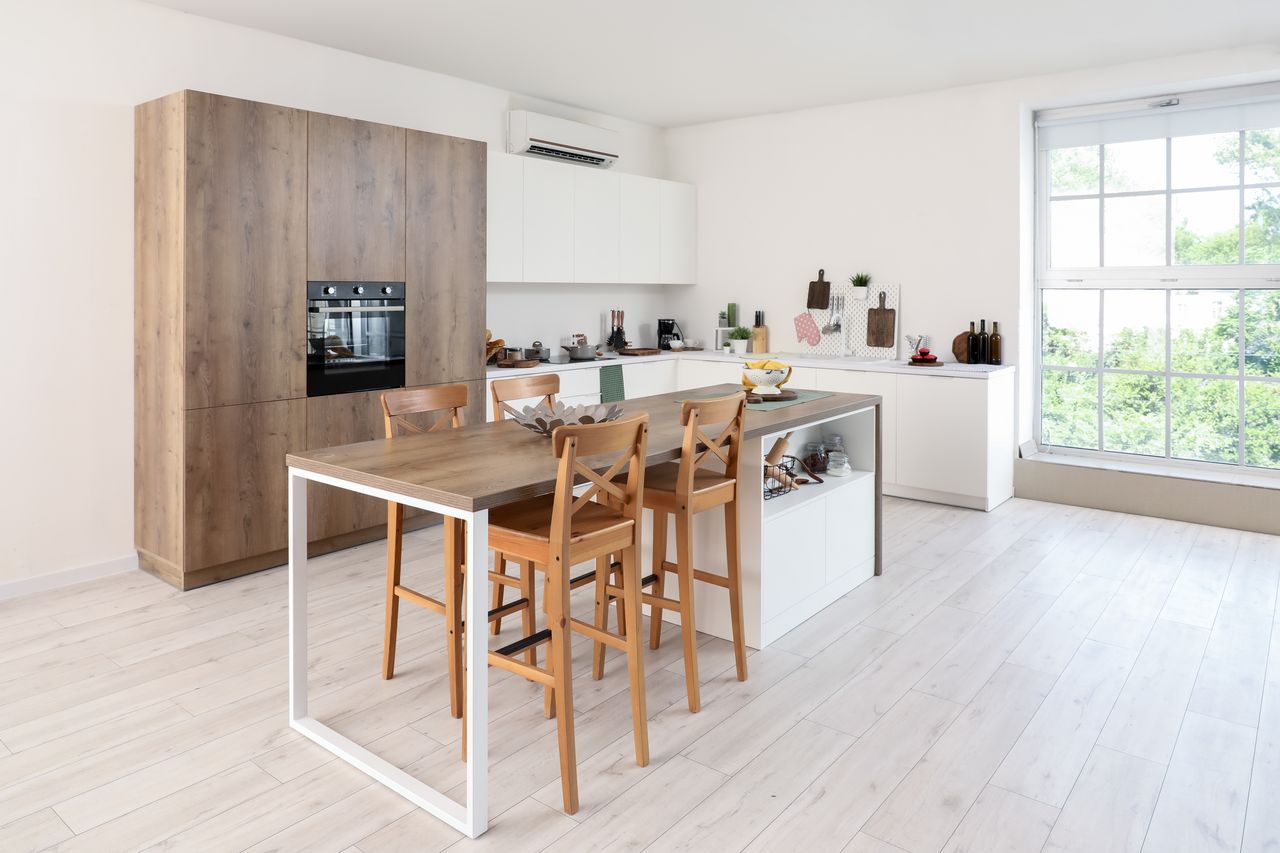 Cuisine compacte lumineuse avec meubles hauts, plan de travail fin, électroménager intégré et îlot en bois.