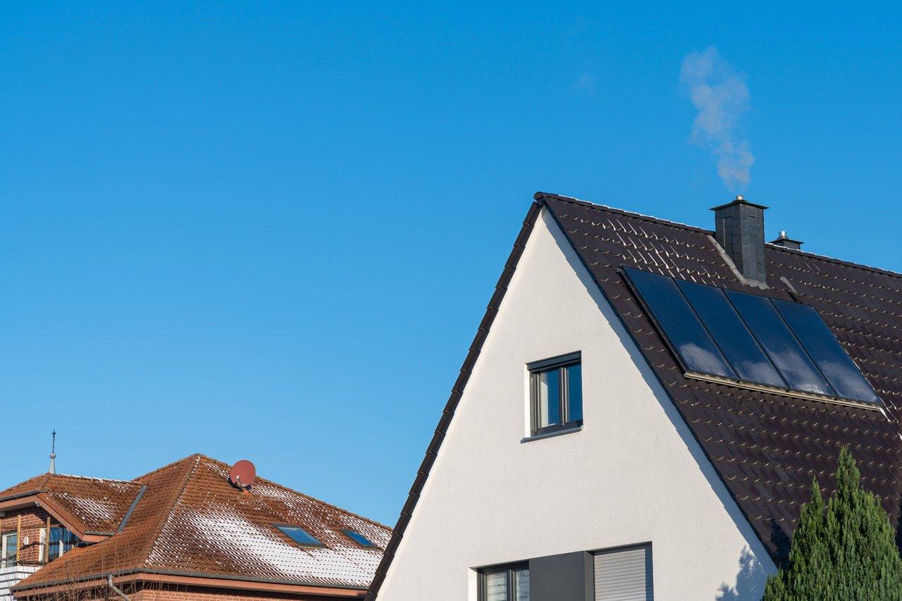 Façade d'une maison RT2012 à haute efficacité énergétique avec cheminée et panneaux solaires.