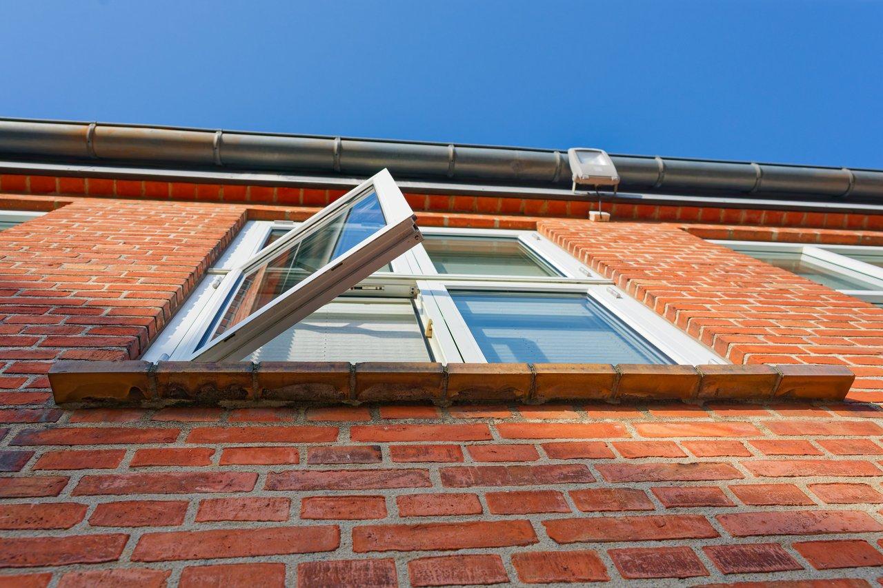 Fenêtre blanche ouverte sur façade en briques rouges pour une ventilation naturelle efficace en période de chauffage.