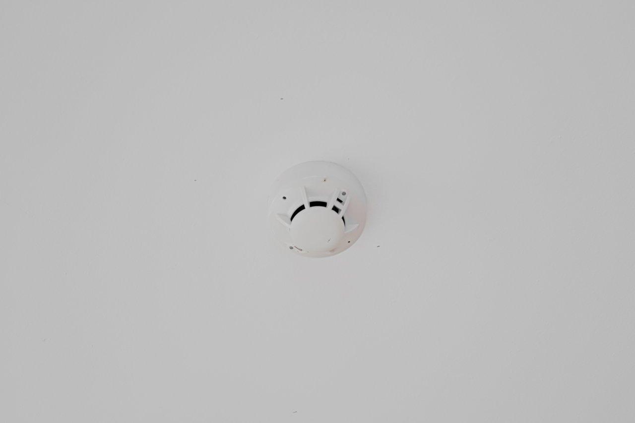 Installation d’un détecteur de fumée au plafond dans un couloir lumineux pour renforcer la sécurité domestique.