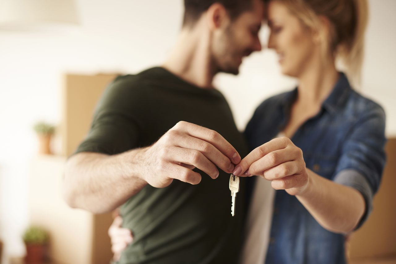 Jeune couple tenant la clé de son nouveau logement, cartons de déménagement en arrière-plan