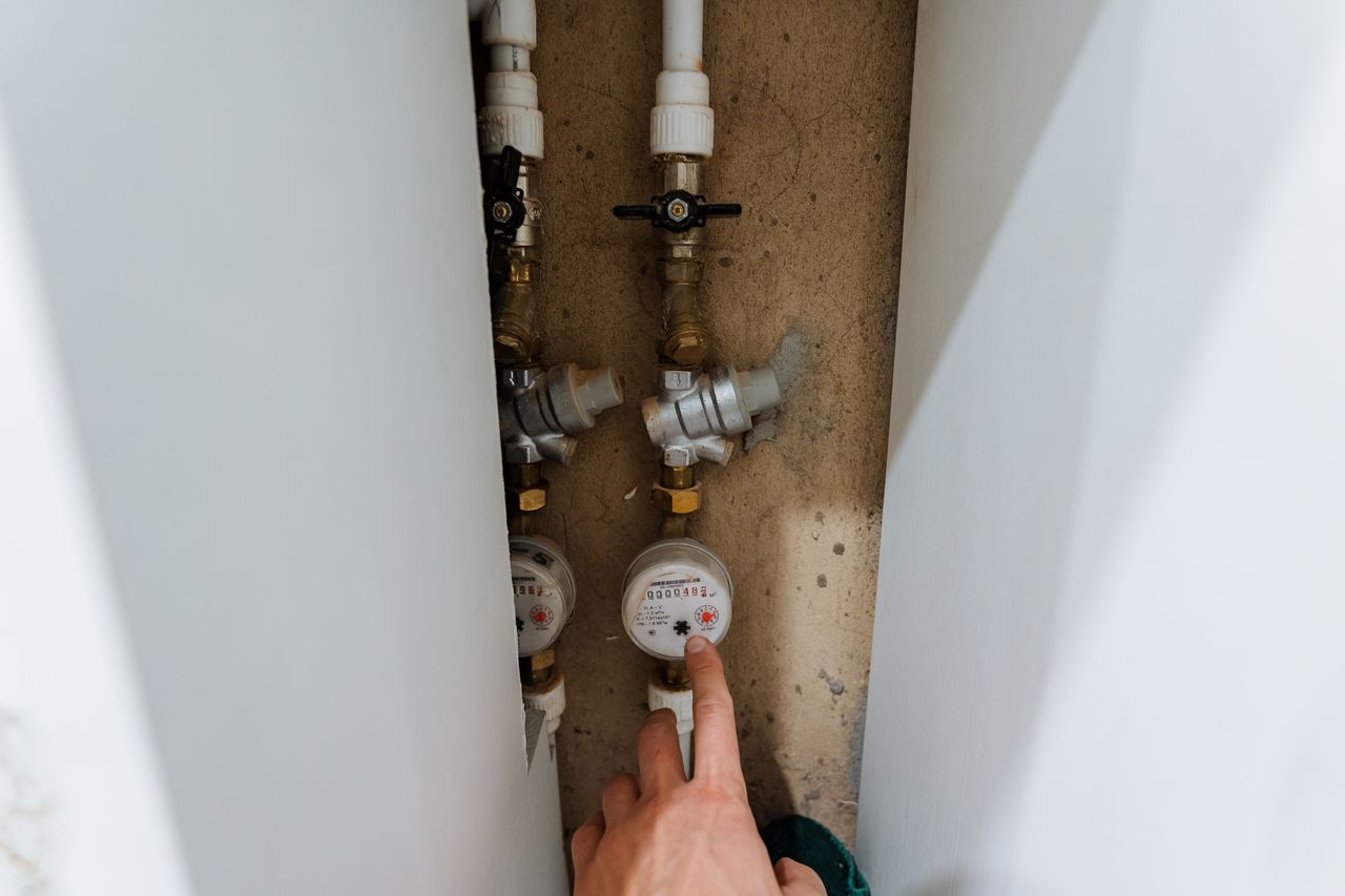 Main inspectant le compteur d’eau domestique près du robinet, de la chasse d’eau et du chauffe-eau.