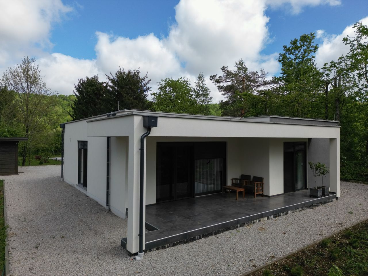 Maison de 100 m² écoénergétique avec pompe à chaleur extérieure, poêle à granulés et bûches rangées près d’un abri