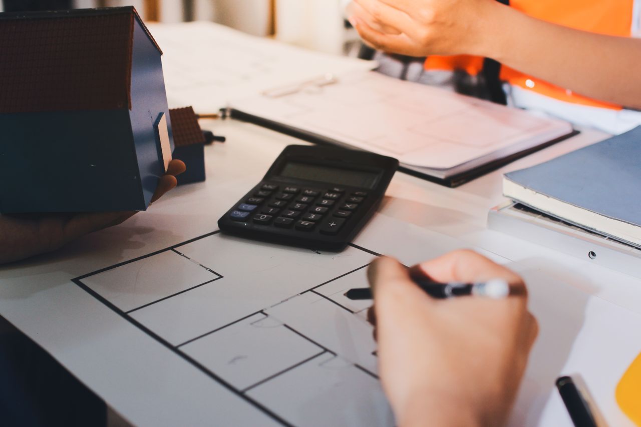 Maison neuve en construction avec calculatrice, plans et dossier de prêt sur une table.