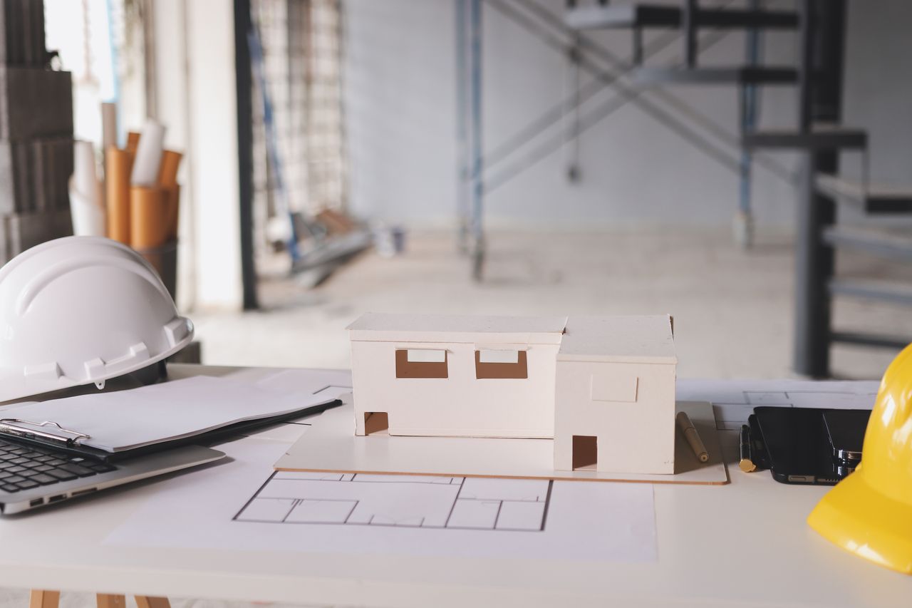 Maison neuve en construction avec plans, calculatrice et casque de chantier sur une table.