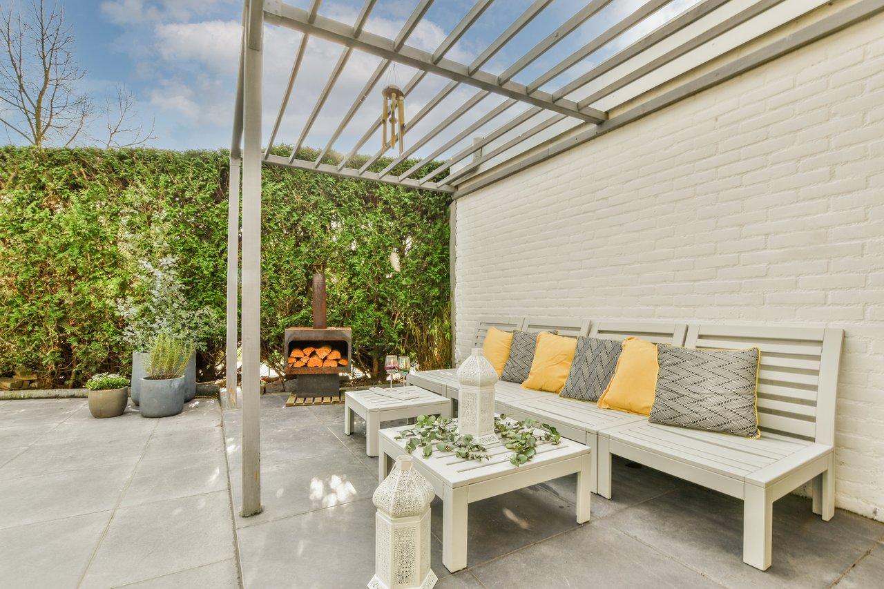 Patio ombragé avec pergola blanche et mobilier d'extérieur, idéal pour rafraîchir passivement en été.
