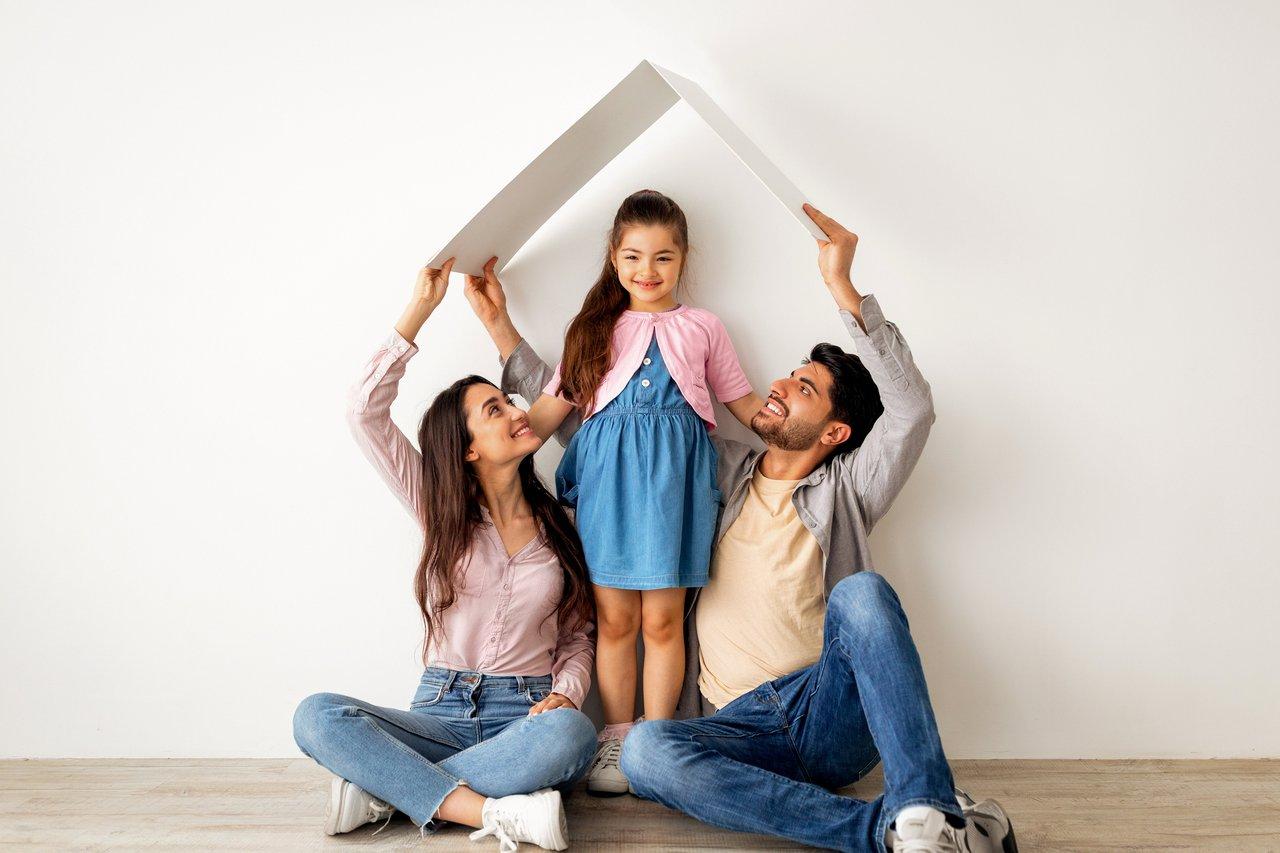 Une jeune famille heureuse devant leur nouvelle maison, symbole de réussite grâce au prêt à Taux Zéro.